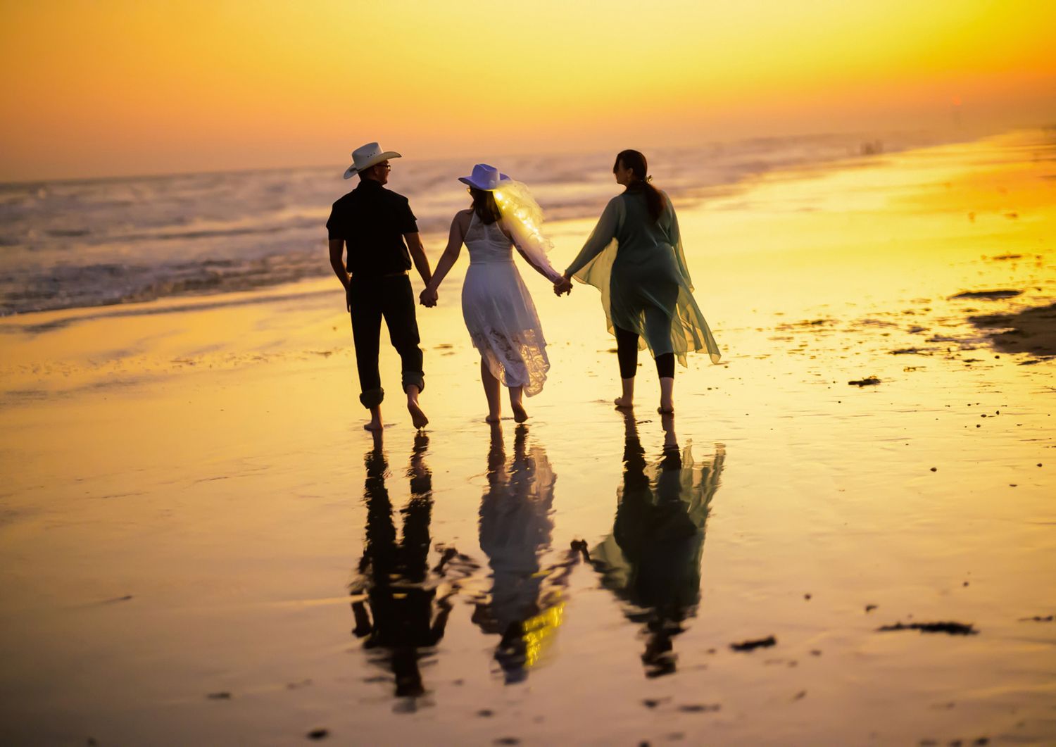 Three people holding hands walk along a golden sunset beach, reflecting on wet sand.