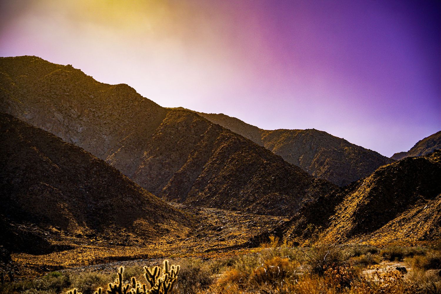 Dramatic desert mountain landscape at dusk with purple and golden sky over rugged canyon terrain.