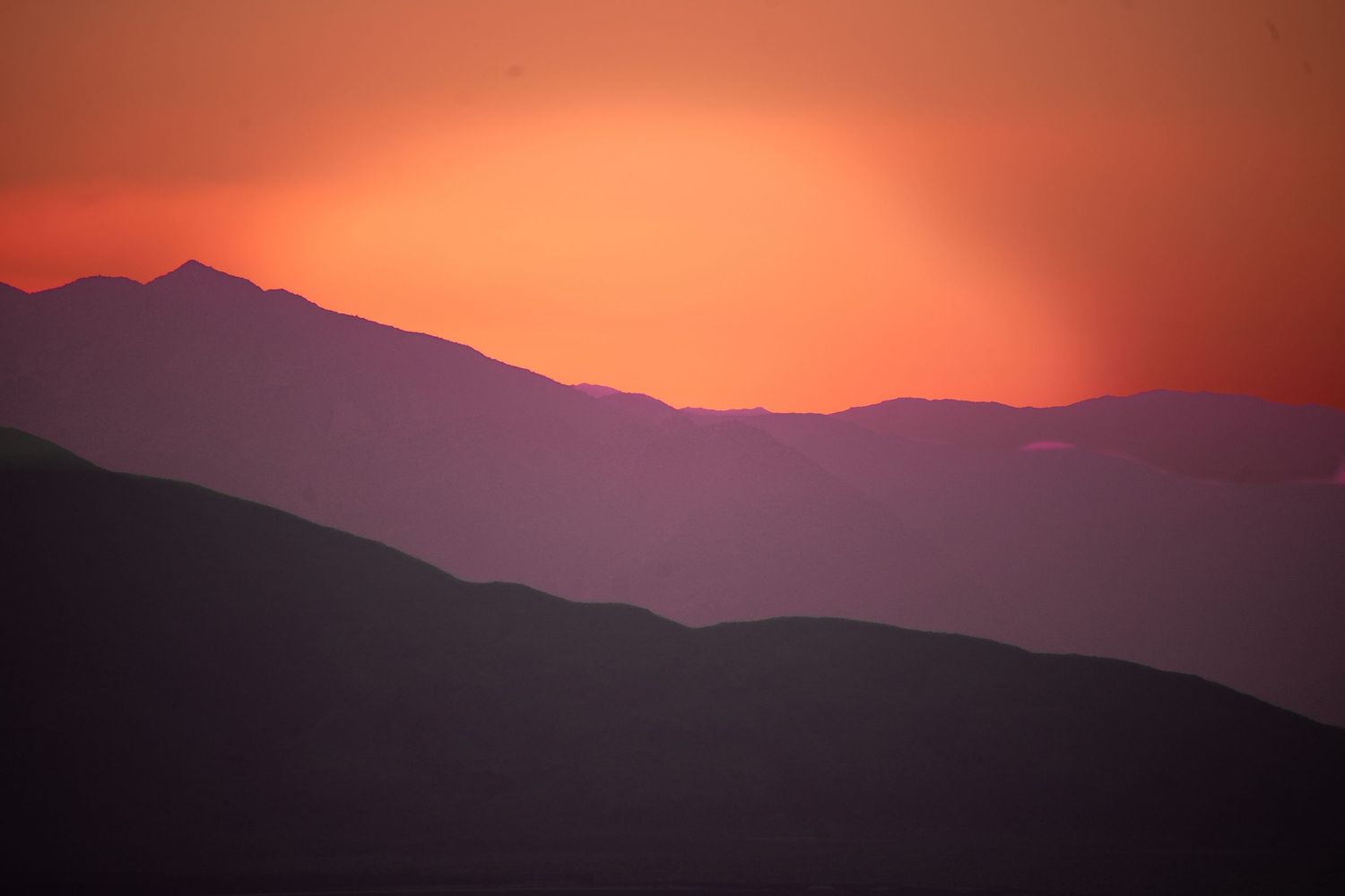 Stunning mountain silhouettes layered against a vivid red and orange sunset sky in a dramatic landscape.