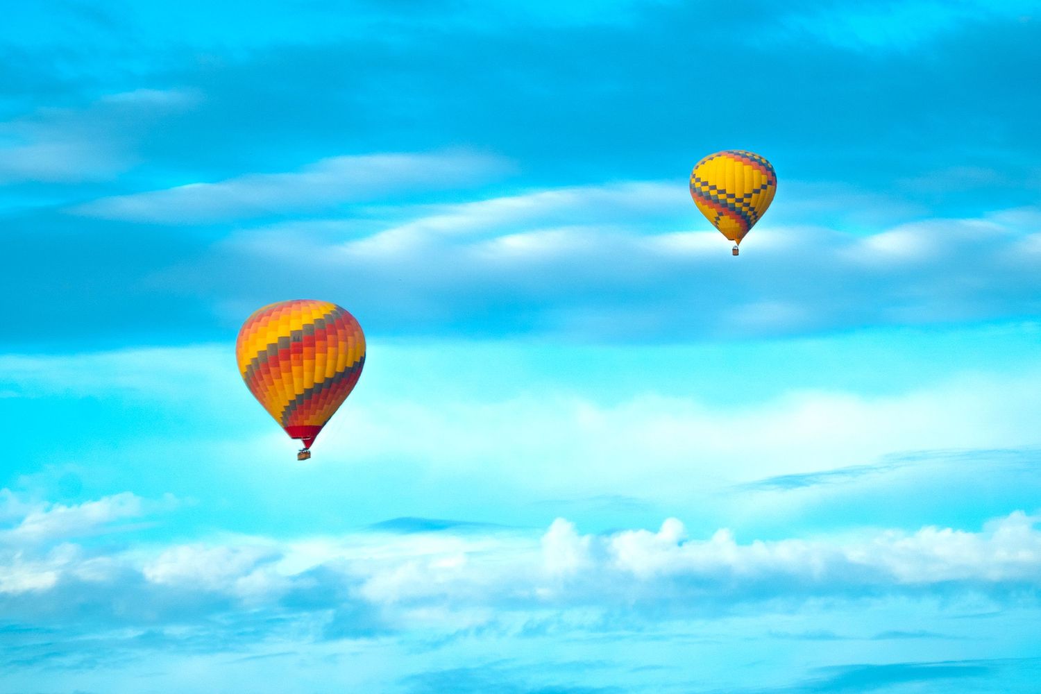 Two colorful hot air balloons soaring through a bright blue sky with fluffy white clouds below.