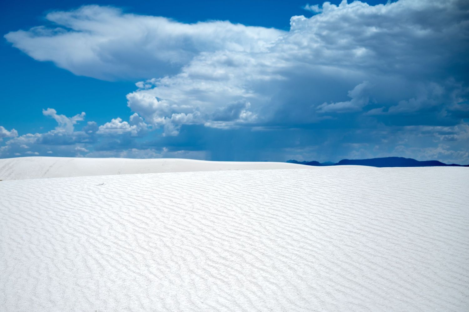 White sand dunes stretch under a vivid blue sky with dramatic clouds at White Sands National Park, New Mexico.