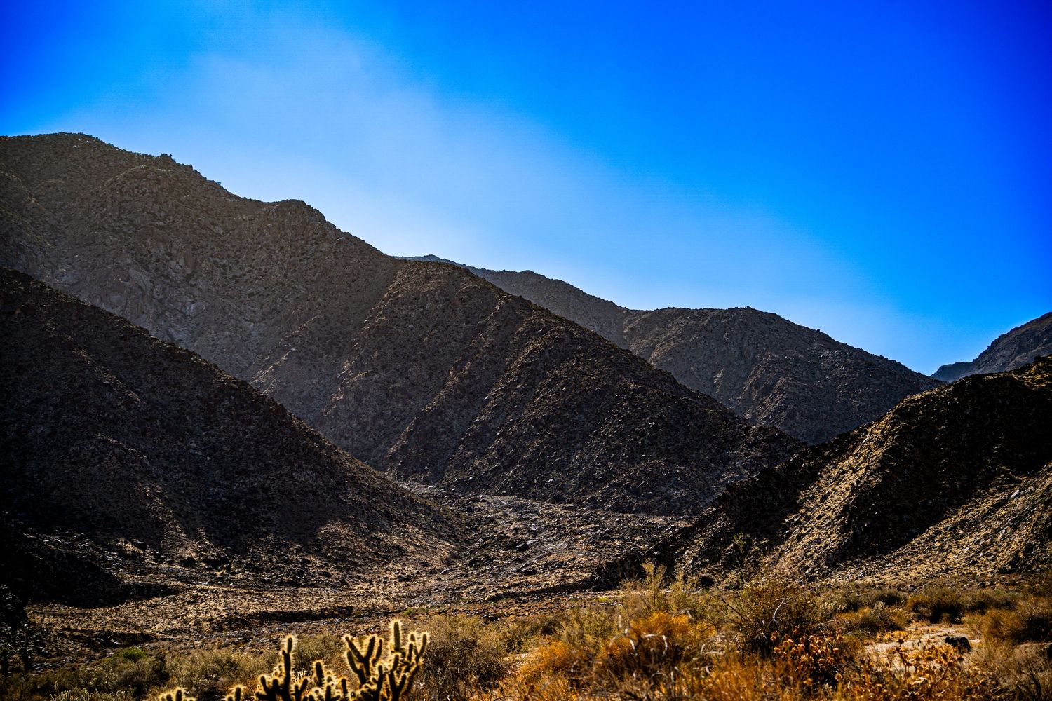 Arid desert mountain valley landscape with sparse vegetation under a clear blue sky.