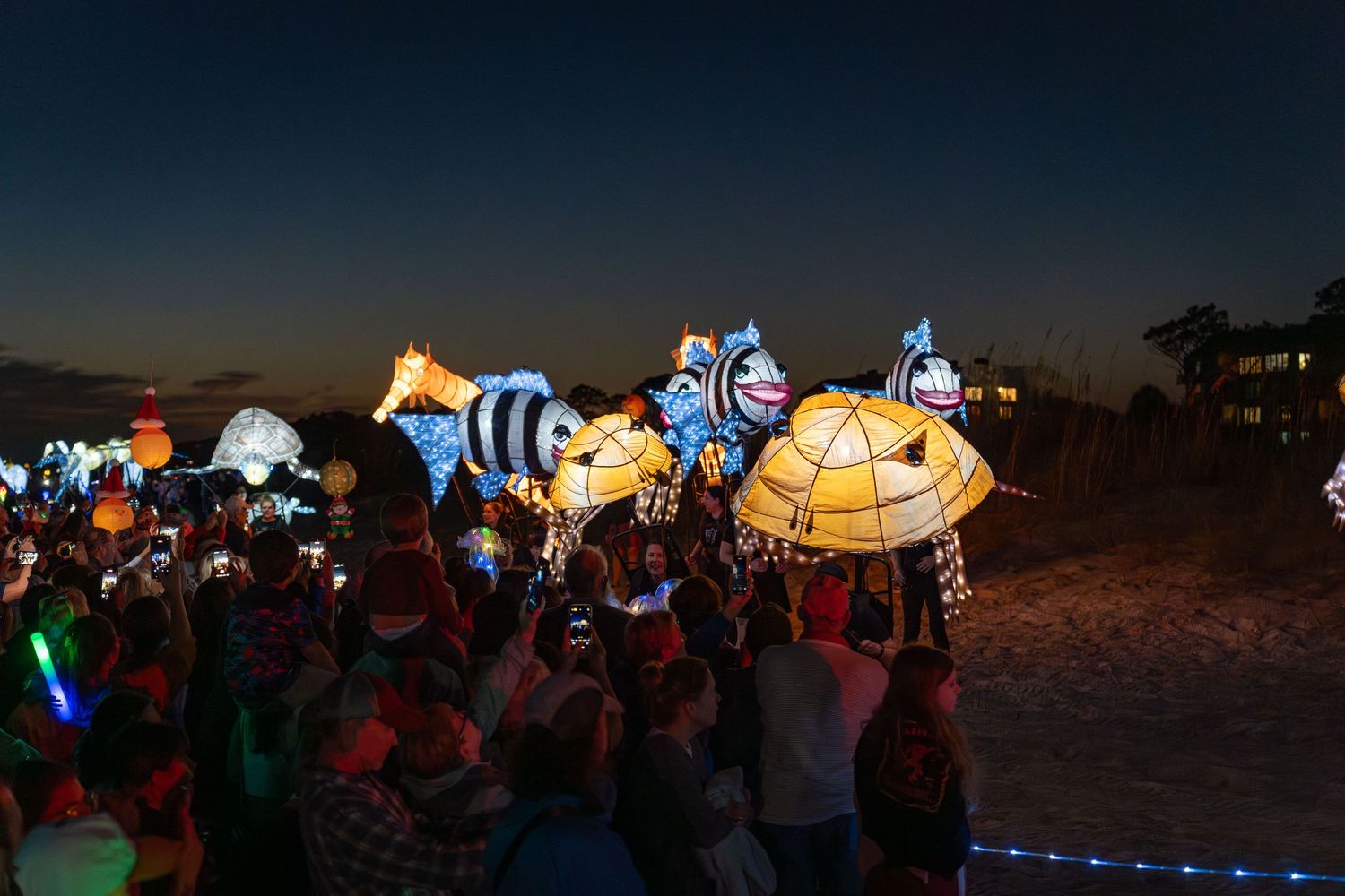 Colorful illuminated fish and sea creatures float past a large beach crowd at the Hilton Head Island Lantern Parade.