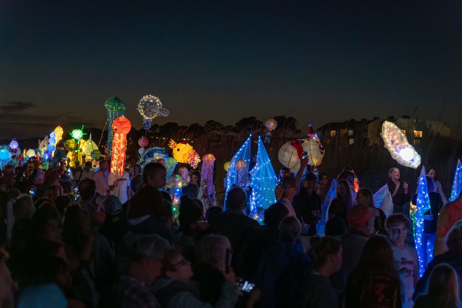 Crowd surrounded by colorful glowing ocean-themed lanterns, including jellyfish and fish, at the Hilton Head Island Lantern Parade.