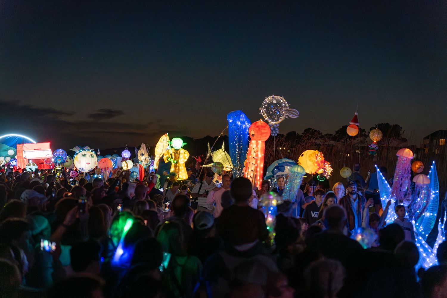 Vibrant illuminated jellyfish, fish, and ocean lanterns glow above a large crowd at the Hilton Head Lantern Parade.