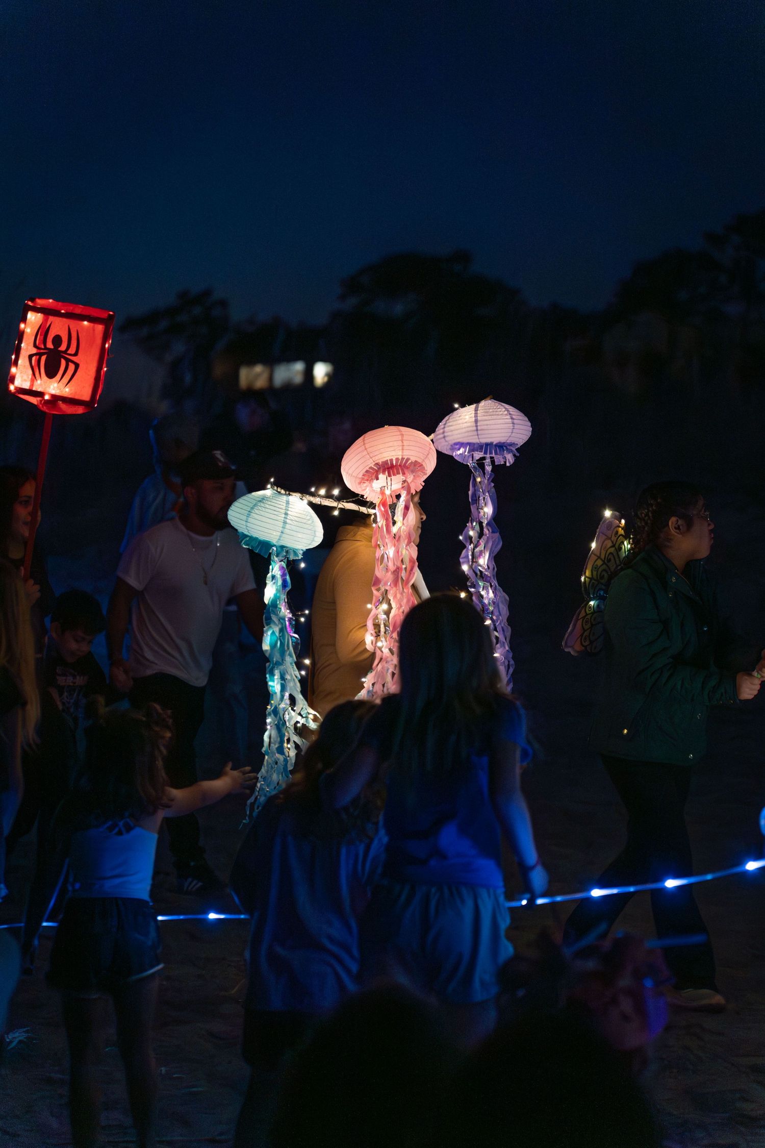 Children and paradegoers walk alongside glowing jellyfish lanterns and a red lantern at the nighttime Hilton Head Lantern Parade.