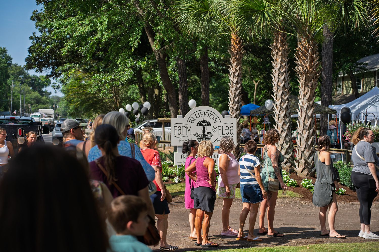 Shoppers walk beneath palm trees toward Bluffton Farm and Flea during the grand opening weekend in Bluffton, South Carolina.