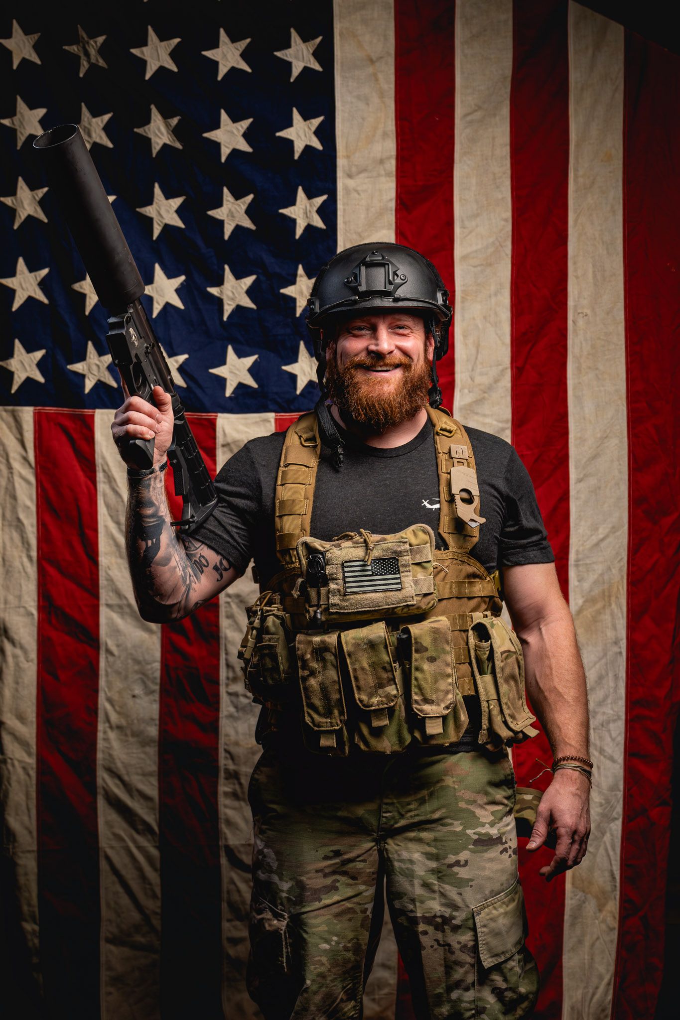 Veteran smiling while posing with tactical gear and Can Cannon in front of a distressed American flag backdrop.