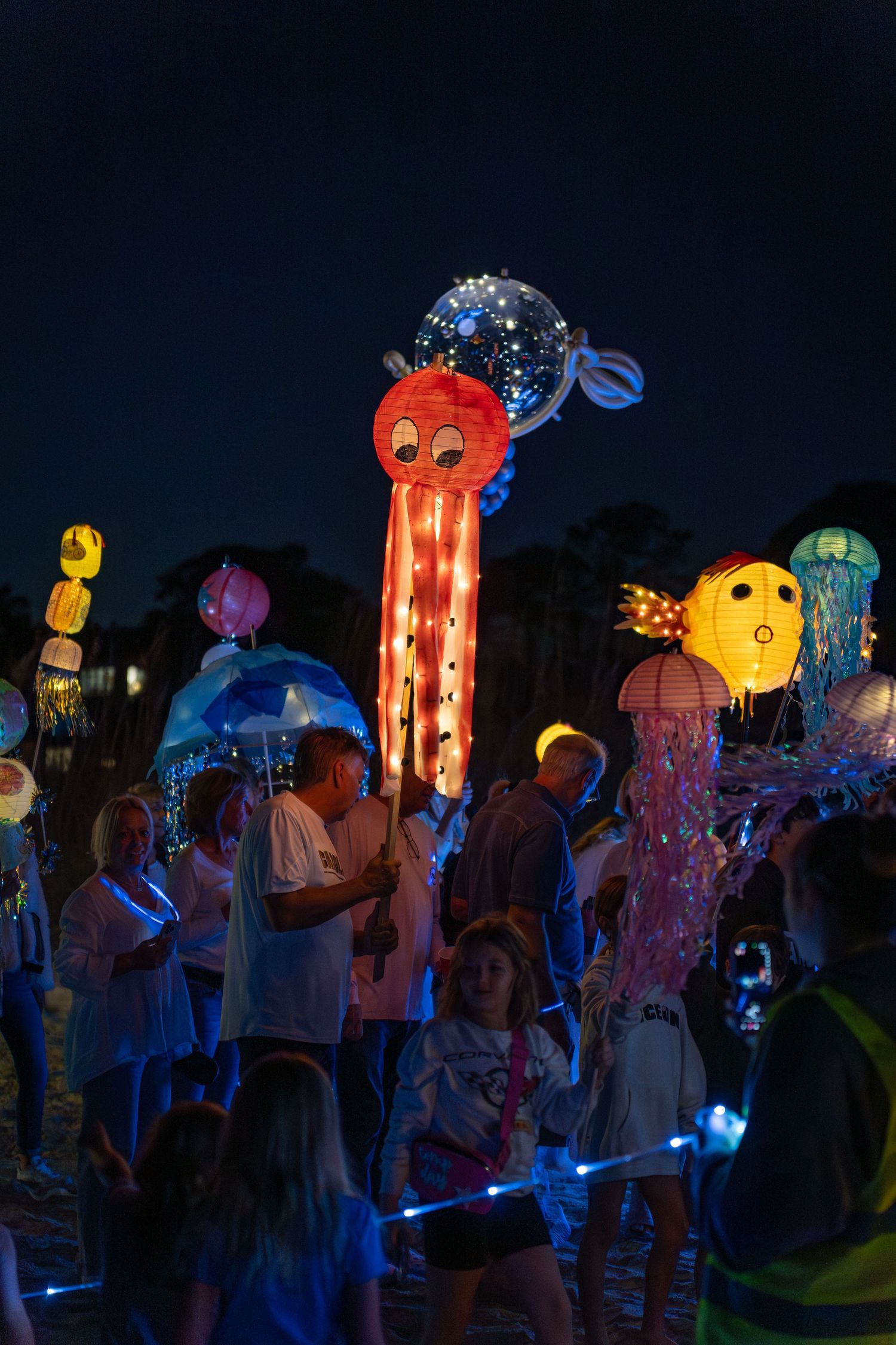 Crowd walking with glowing jellyfish and octopus lanterns during the Hilton Head Island Lantern Parade on the beach at night.