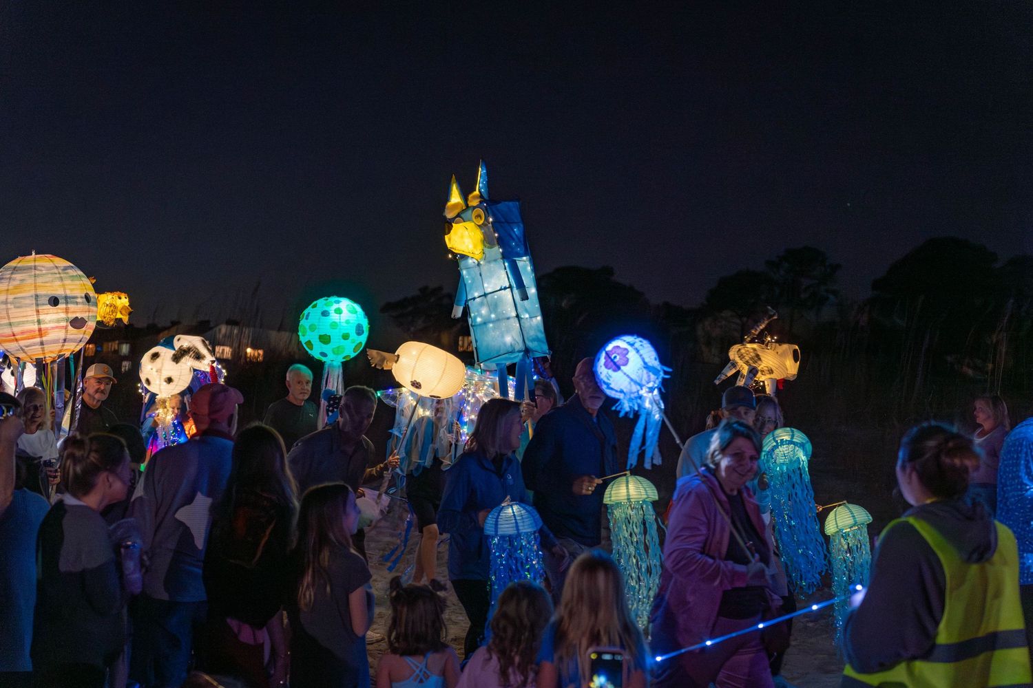 Paradegoers walk with glowing jellyfish and colorful creature lanterns lighting the beach path during the Hilton Head Island Lantern Parade.