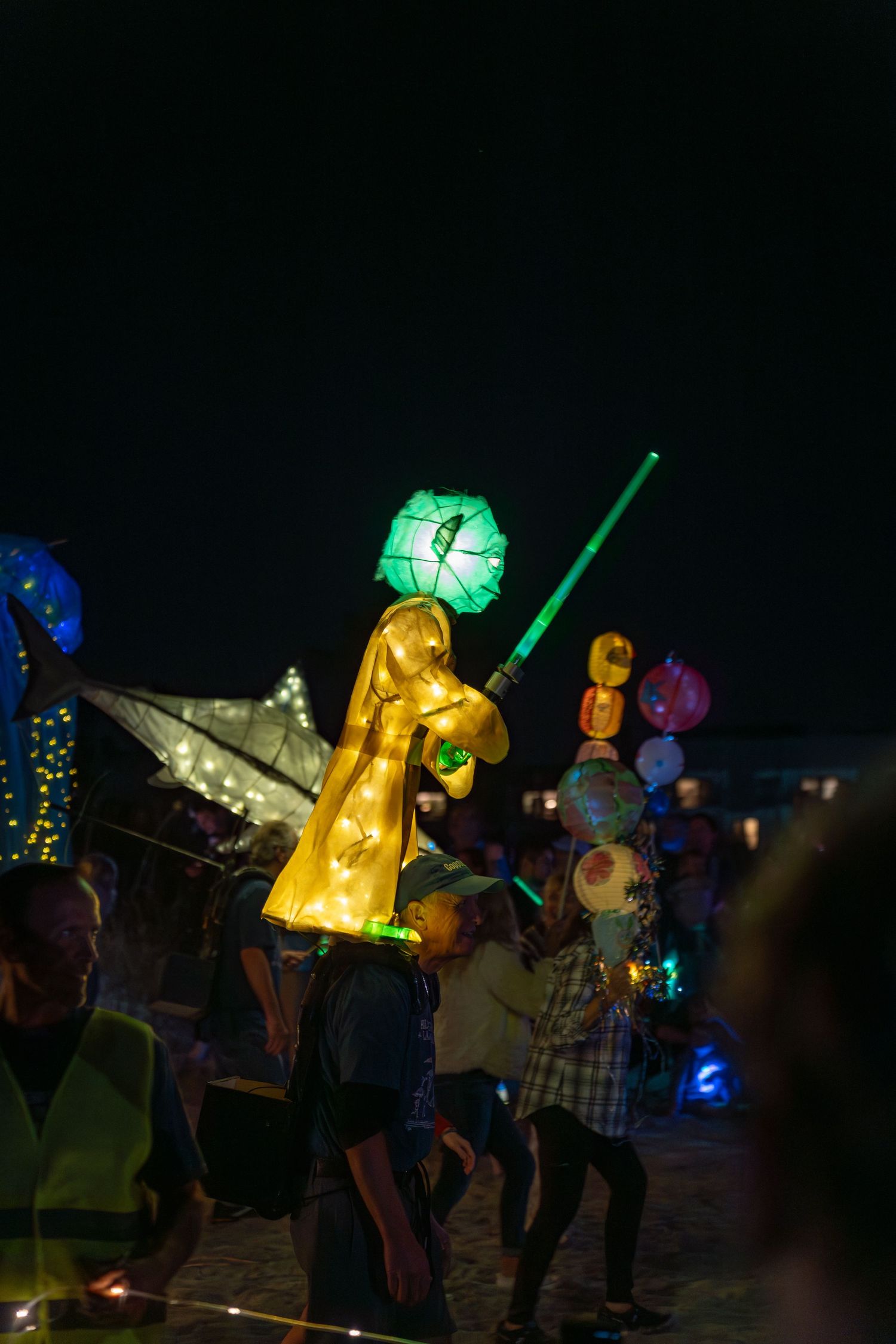 A glowing Yoda lantern holding a green lightsaber is carried along the beach path during the Hilton Head Island Lantern Parade at night.