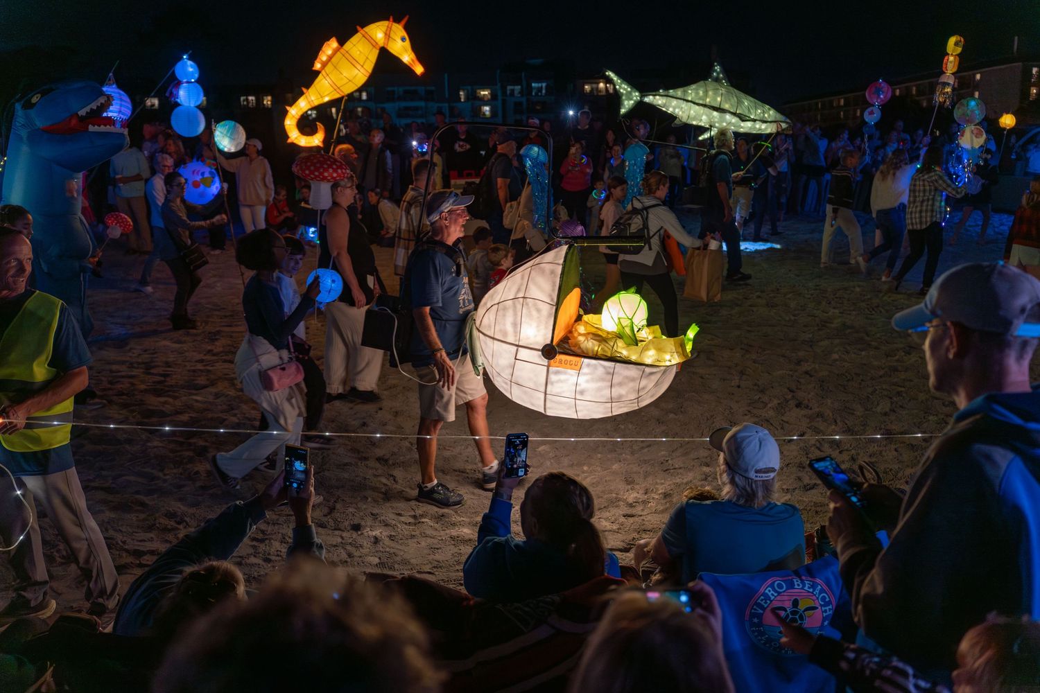A glowing Grogu lantern resting in an illuminated floating pod moves past spectators during the nighttime Hilton Head Island Lantern Parade.