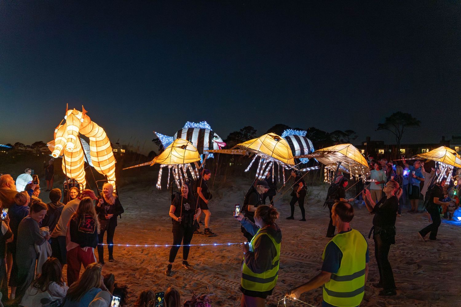 Large illuminated seahorse and glowing fish lanterns carried by performers on the beach during the Hilton Head Lantern Parade.