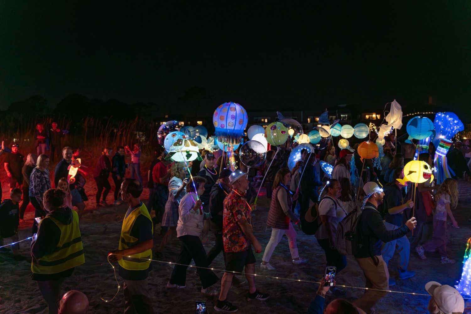Parade walkers carry glowing jellyfish, fish, and ocean-themed lanterns along the beach during the lively Hilton Head Lantern Parade.