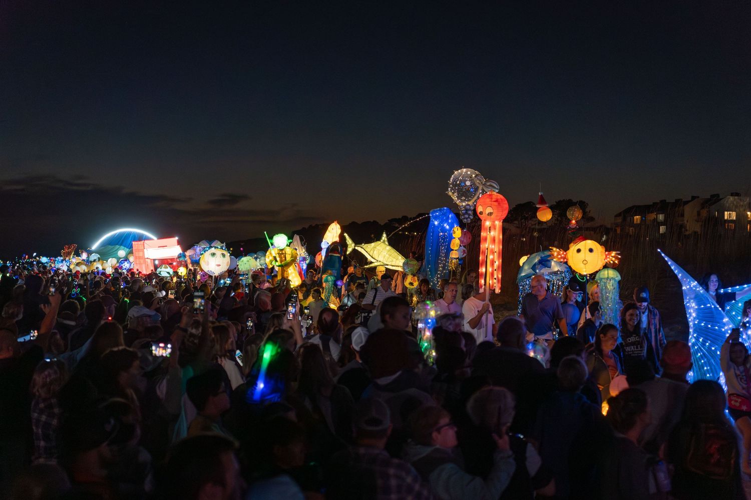 Crowds gather on the Hilton Head beach at dusk as colorful glowing ocean-themed lanterns light the shoreline during the Lantern Parade.