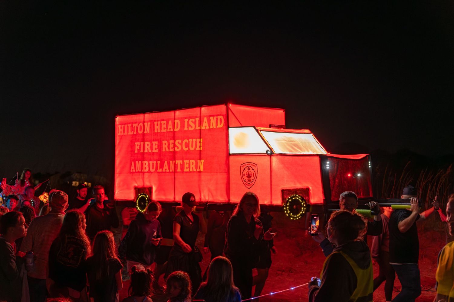 A giant glowing red lantern shaped like a fire rescue vehicle labeled “Ambulantern” is carried by volunteers at the Hilton Head Parade.