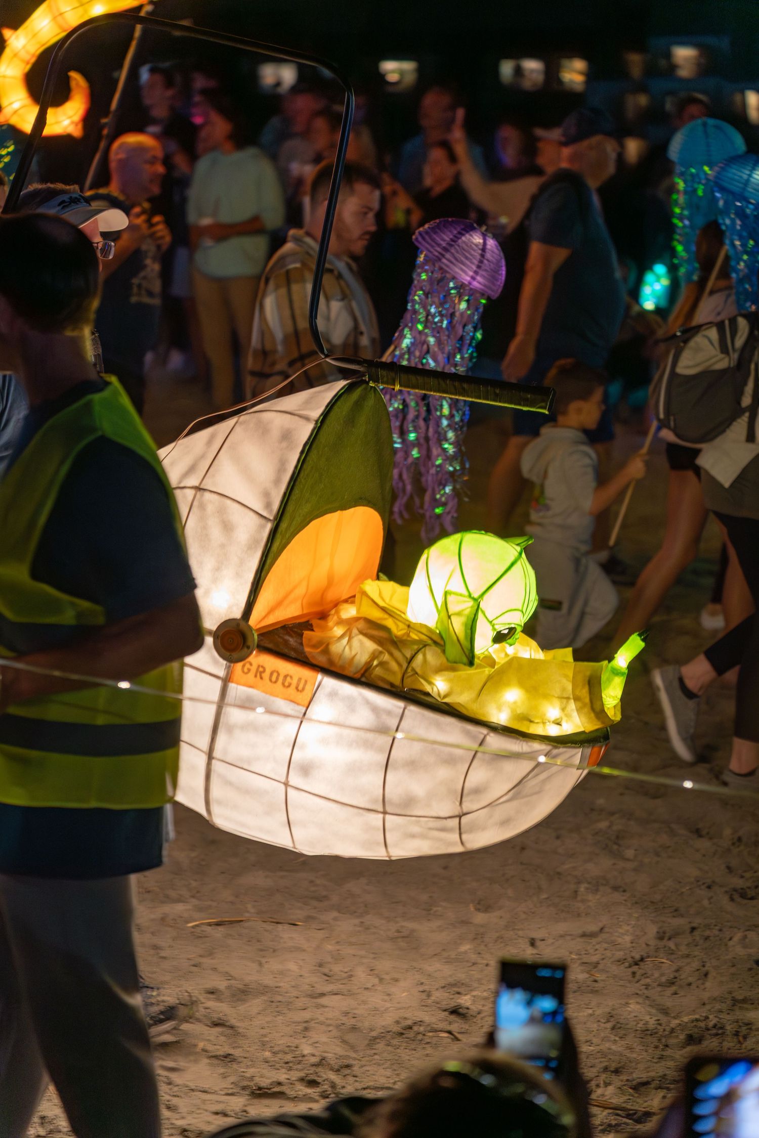 Families watch a glowing Grogu lantern in a light-filled pod surrounded by sea-creature lanterns during the Hilton Head Lantern Parade.