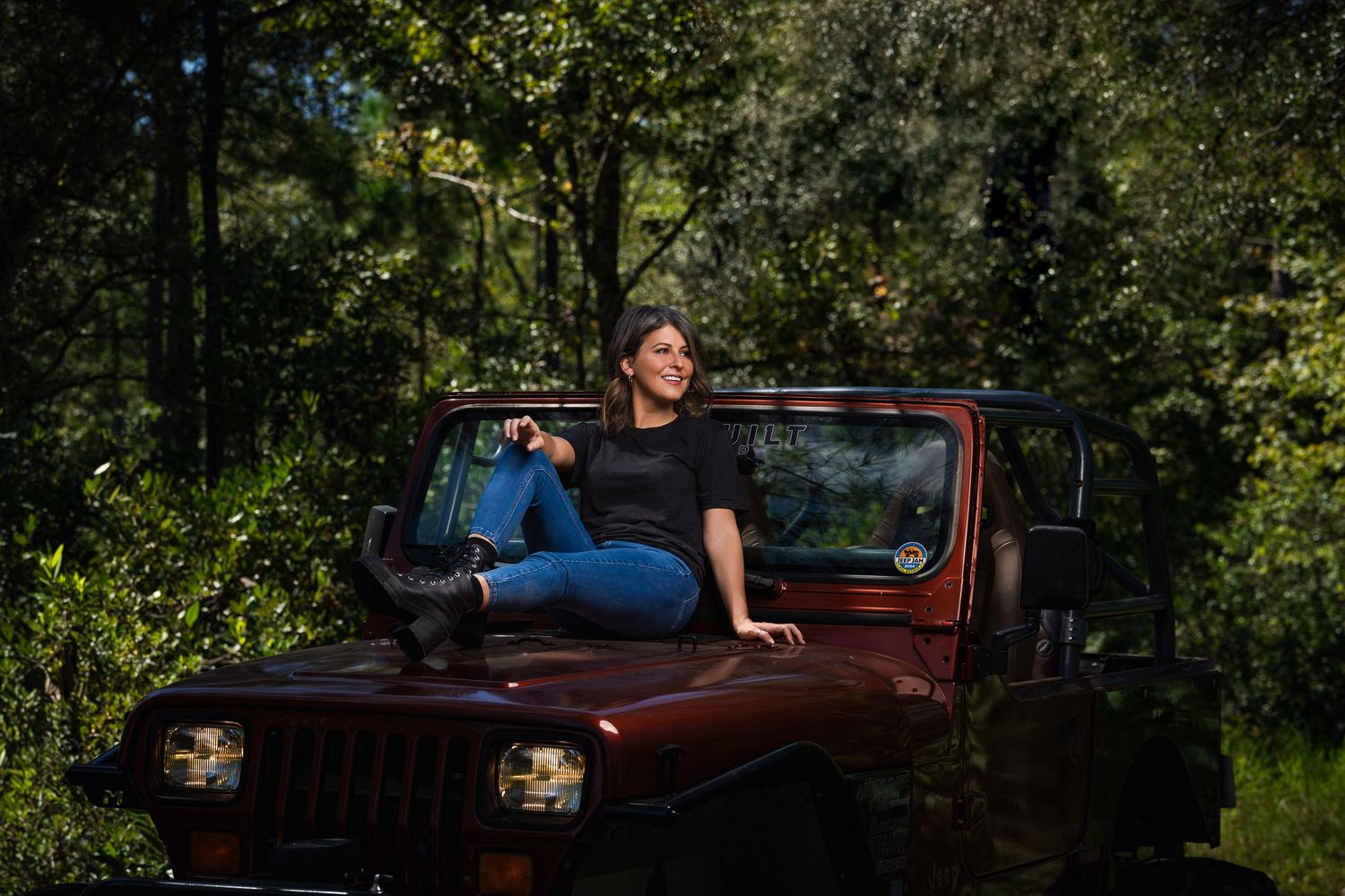 Lifestyle portrait photography of a woman posing on a Jeep outdoors surrounded by natural greenery captured by GoodnRich Photography