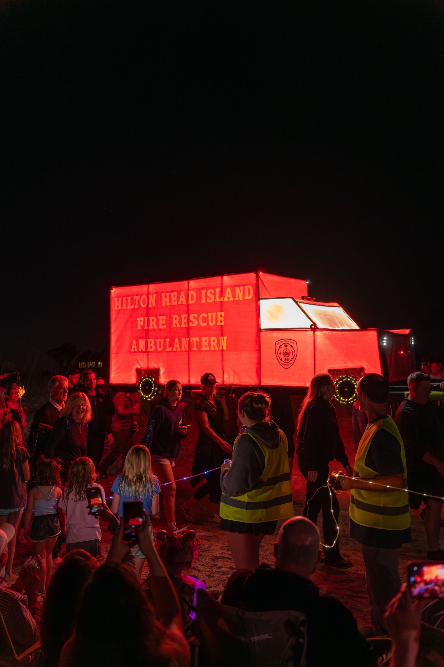 Spectators watch the bright red “Hilton Head Fire Rescue Ambulantern” lantern float by during the nighttime Hilton Head Island Parade.