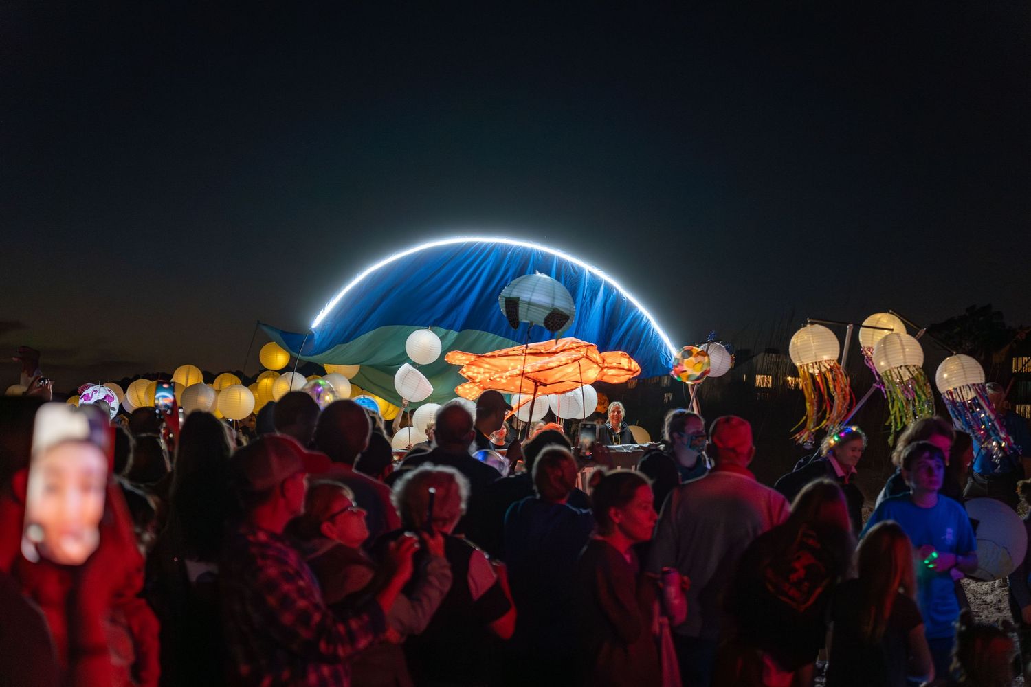 A glowing sea turtle lantern hovers above the crowd as colorful jellyfish and ocean lanterns light the night at the Hilton Head Parade.