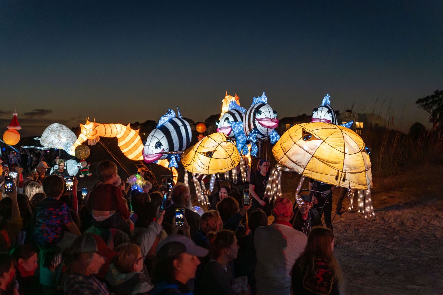 Striped glowing fish and bright lantern sculptures move along the beach as families gather to watch the Hilton Head parade.