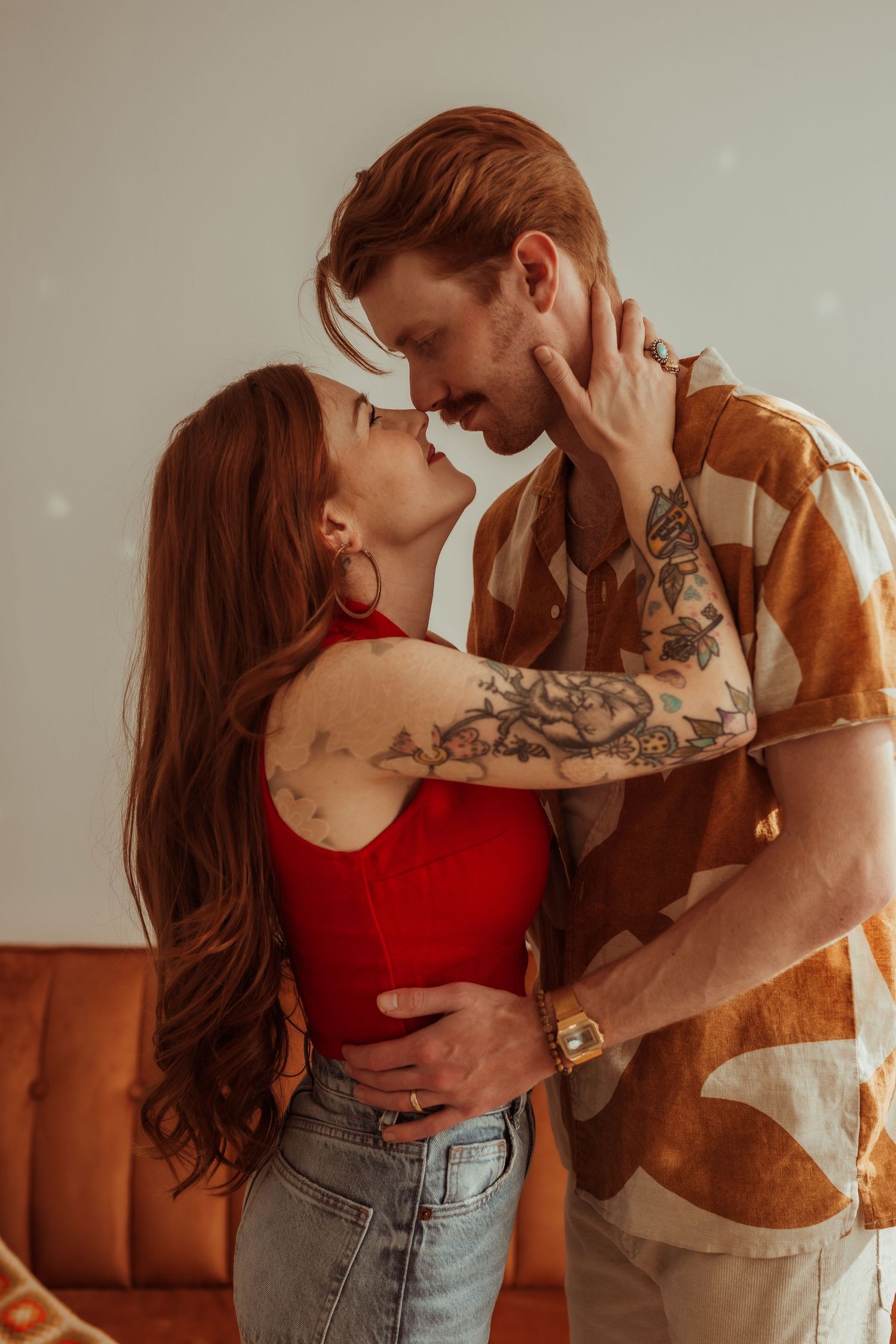 Tattooed couple leaning in for a kiss in a warmly lit vintage-inspired indoor setting. Tulsa Photographer