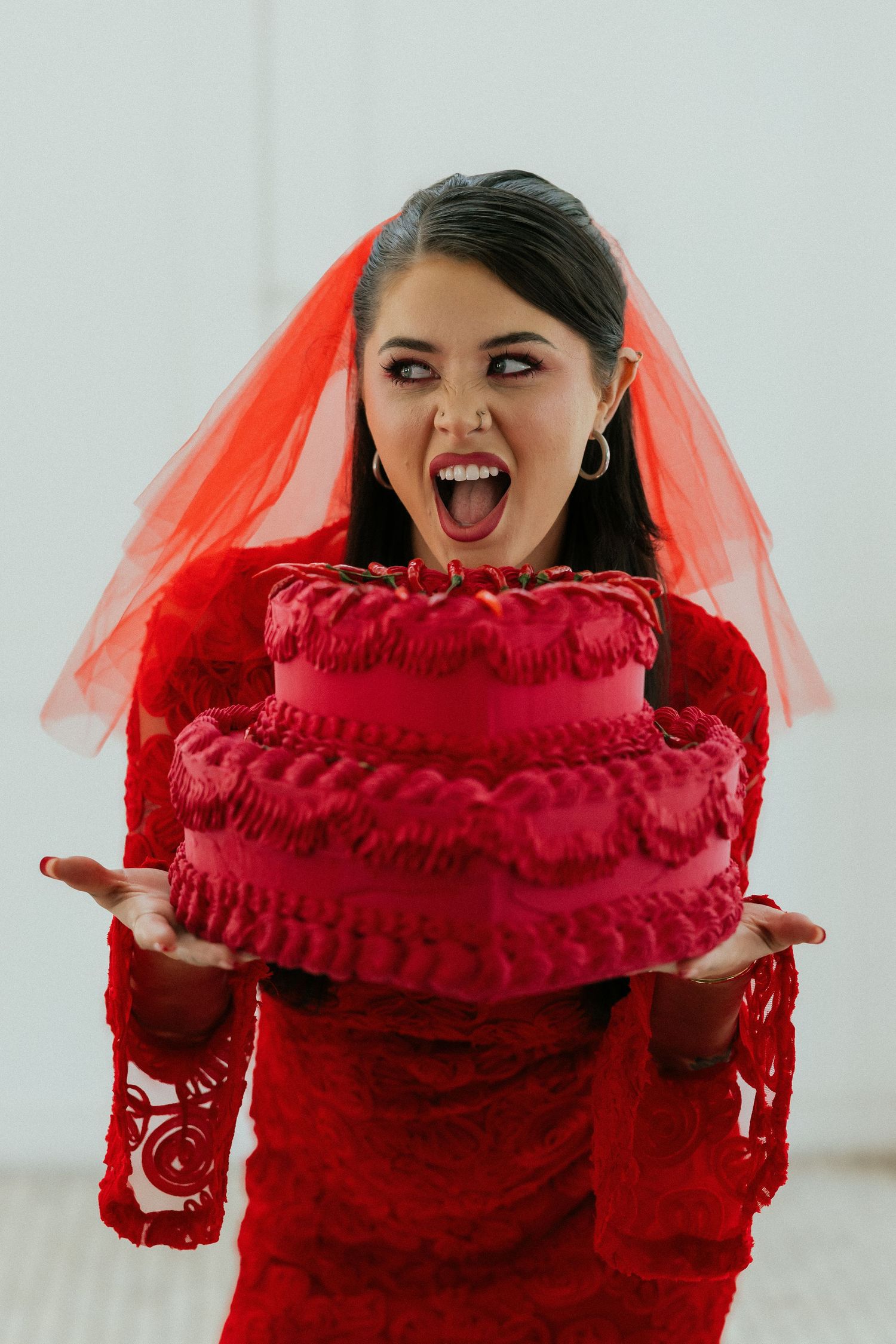 Excited woman in red lace dress and red veil holding a decorative red ruffled cake prop. Tulsa Photographer