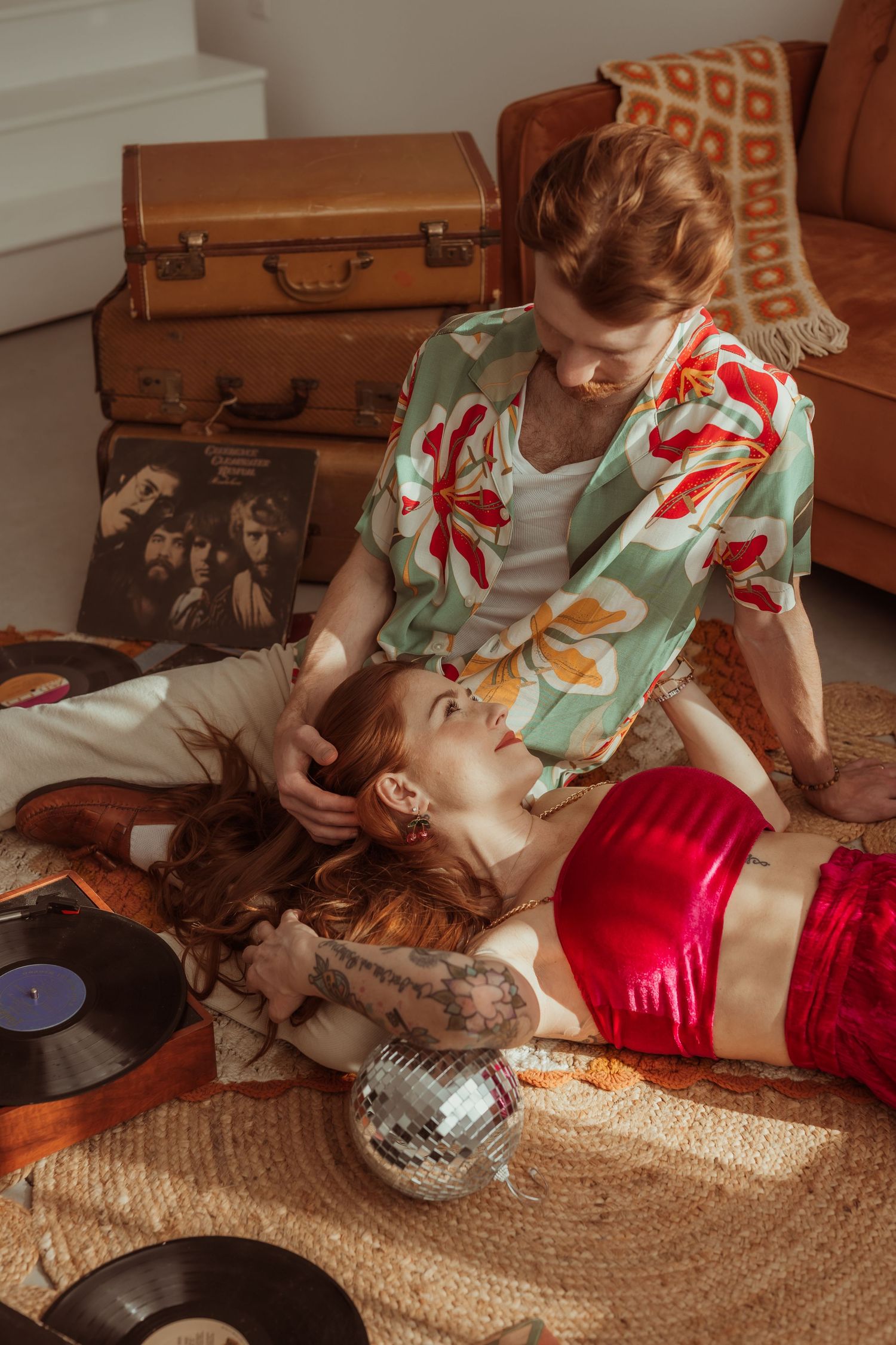 Couple with tattoos sharing a romantic retro-styled moment surrounded by vinyl records and luggage. Tulsa Photographer