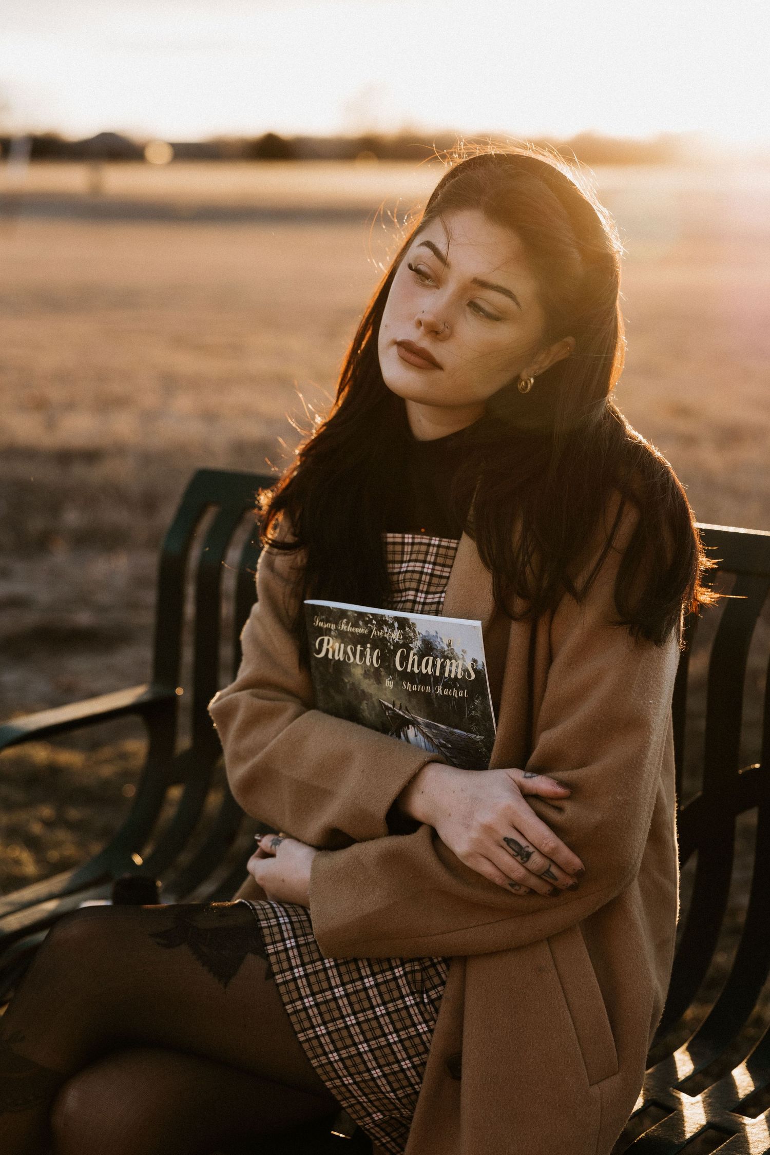 Woman holding a book titled Rustic Charms while sitting on a bench at golden hour sunset. Tulsa Photographer