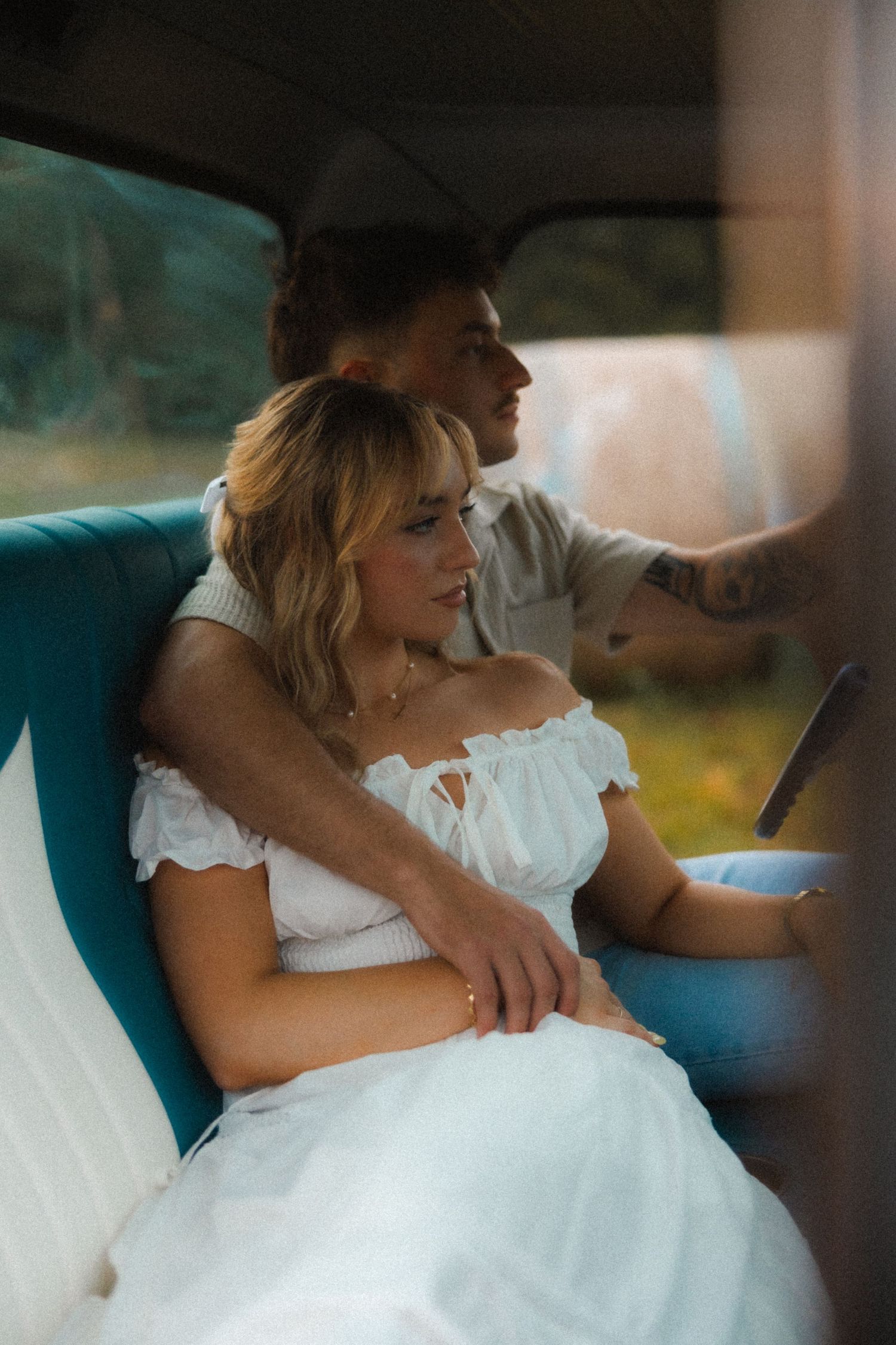 Romantic couple sitting in a vintage vehicle, woman in white off-shoulder dress leaning against her partner. Tulsa Photographer