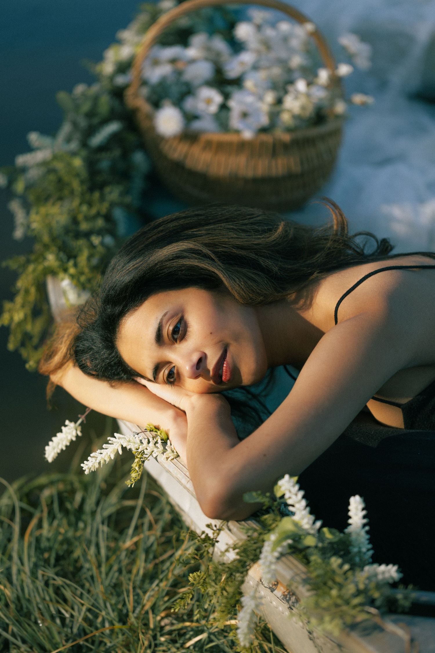 Young woman lying among white wildflowers and wicker basket, bathed in warm golden light. Tulsa Photographer