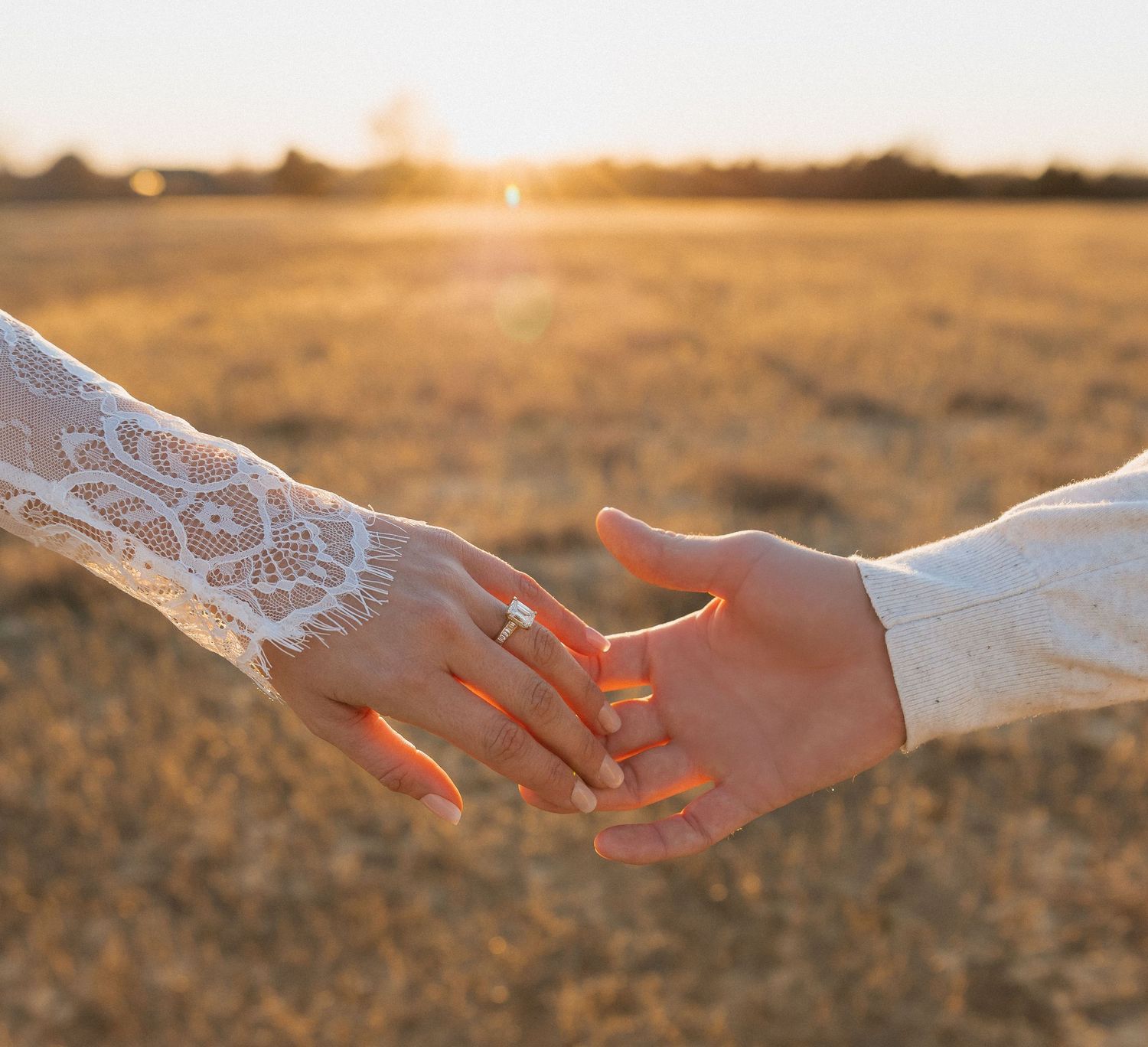 Close-up of couple holding hands at sunset in golden field, bride wearing lace sleeve with ring. Tulsa Photographer