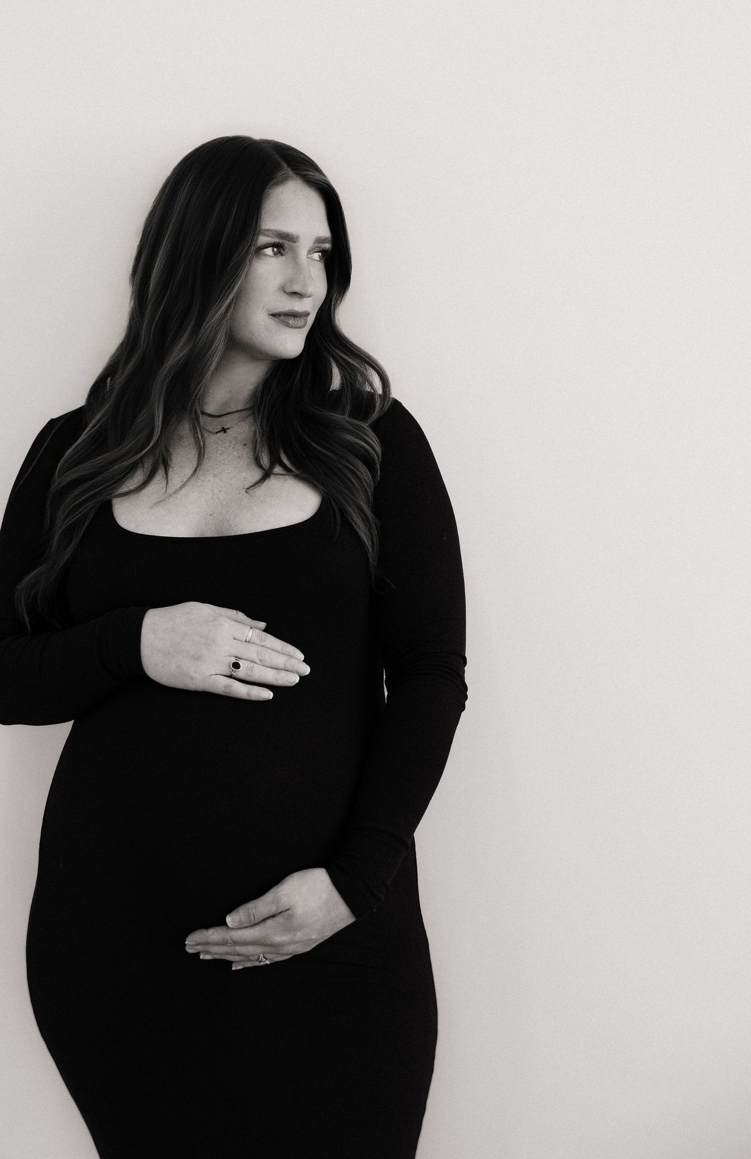 Pregnant woman in black dress cradling baby bump, elegant maternity portrait in black and white.