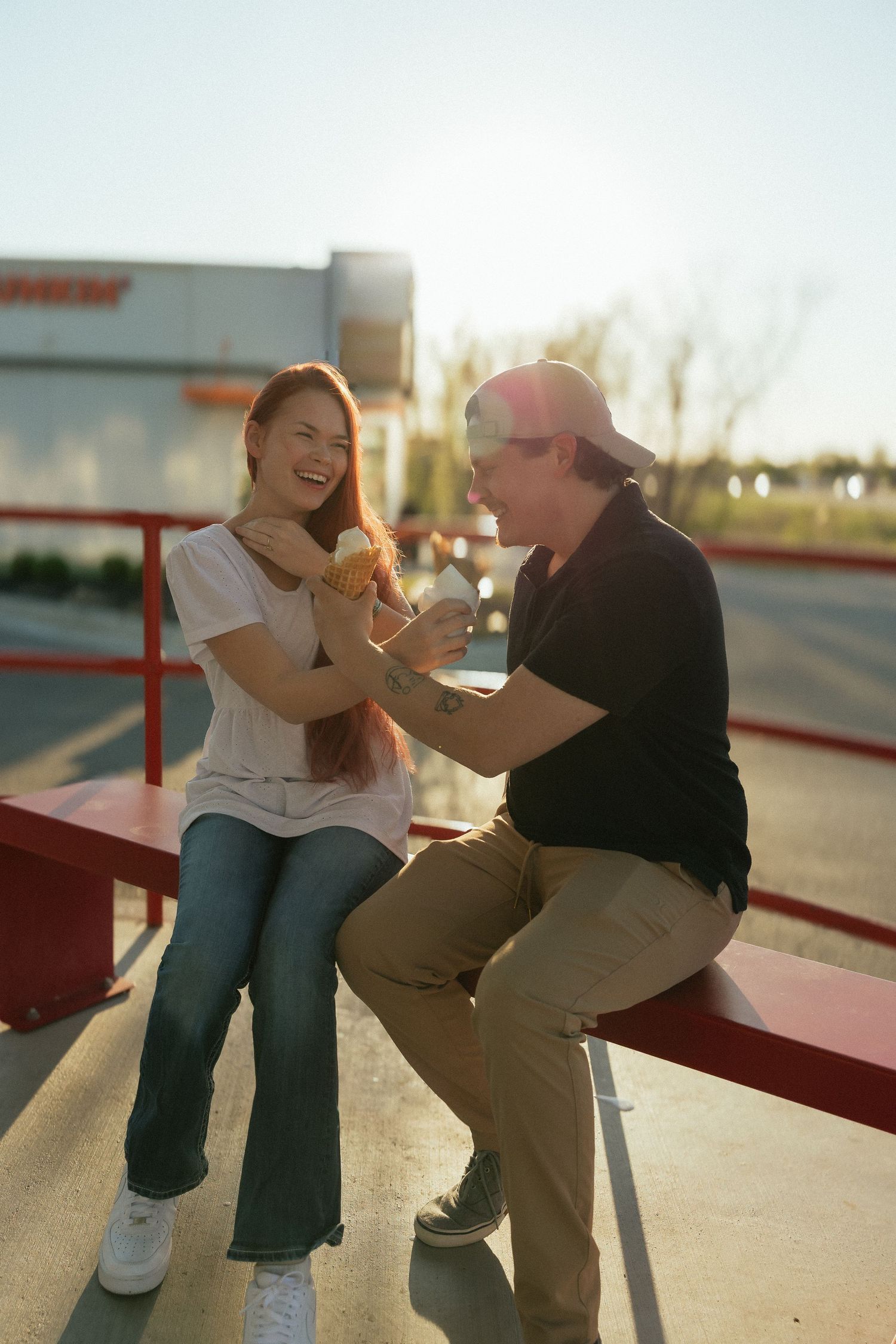 A laughing couple shares a joyful moment on red bleachers outside a Dunkin restaurant at golden hour. Tulsa Photographer