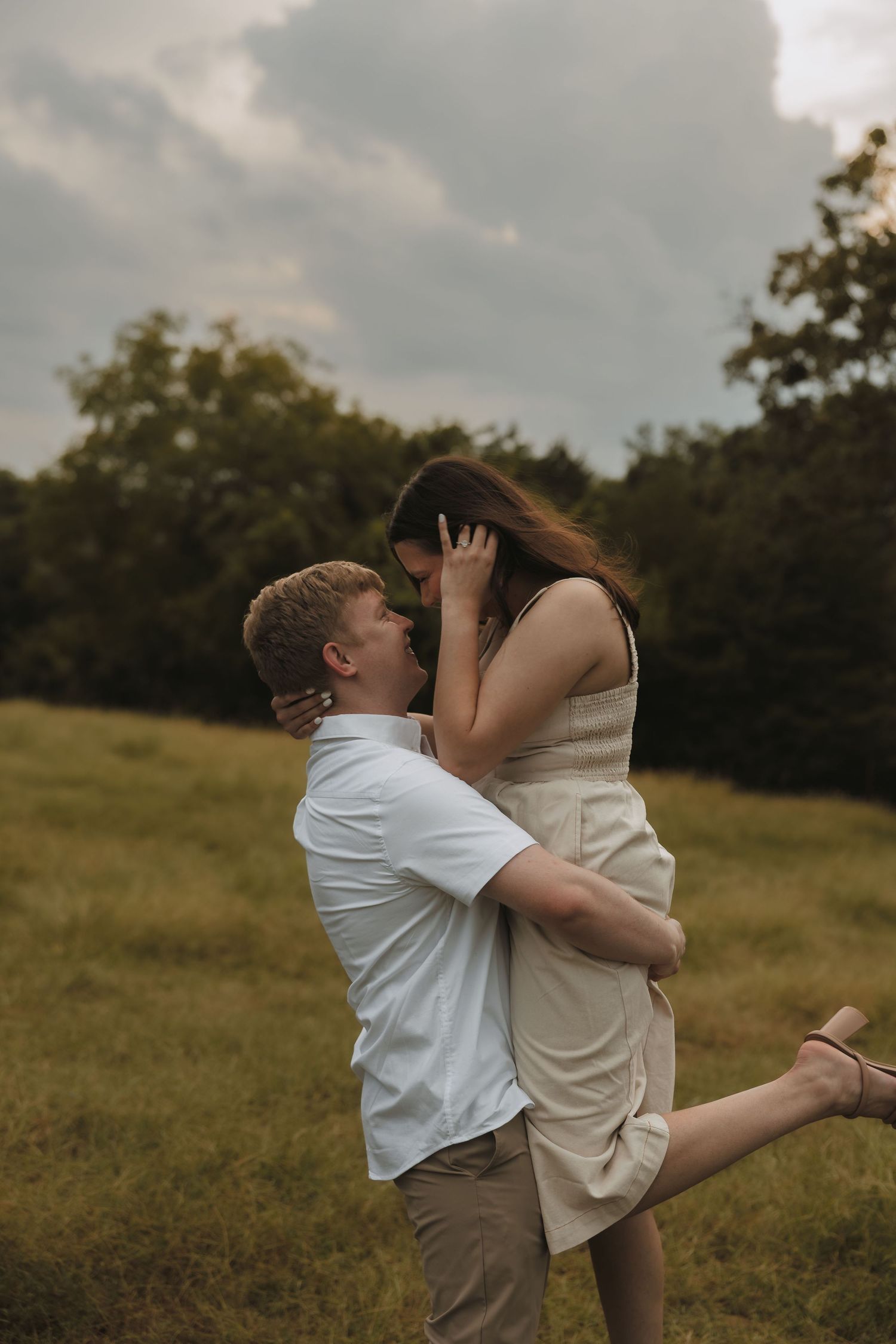 A couple shares a romantic moment in a green field, the man lifting the woman as they lean in for a kiss. Tulsa Photographer