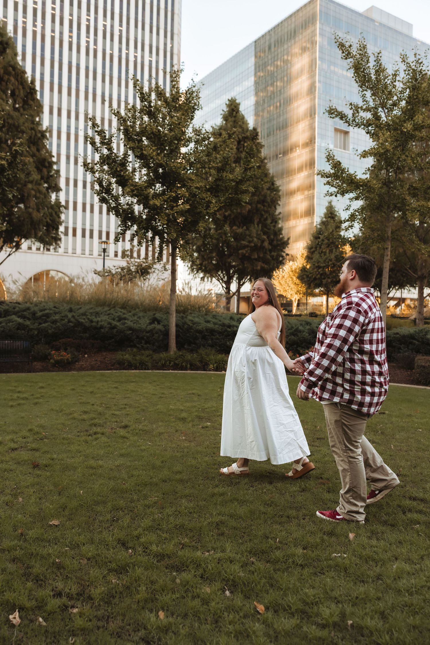 Couple holding hands walking through urban park in wedding attire, bride in white dress, groom in plaid shirt. Tulsa Photographer