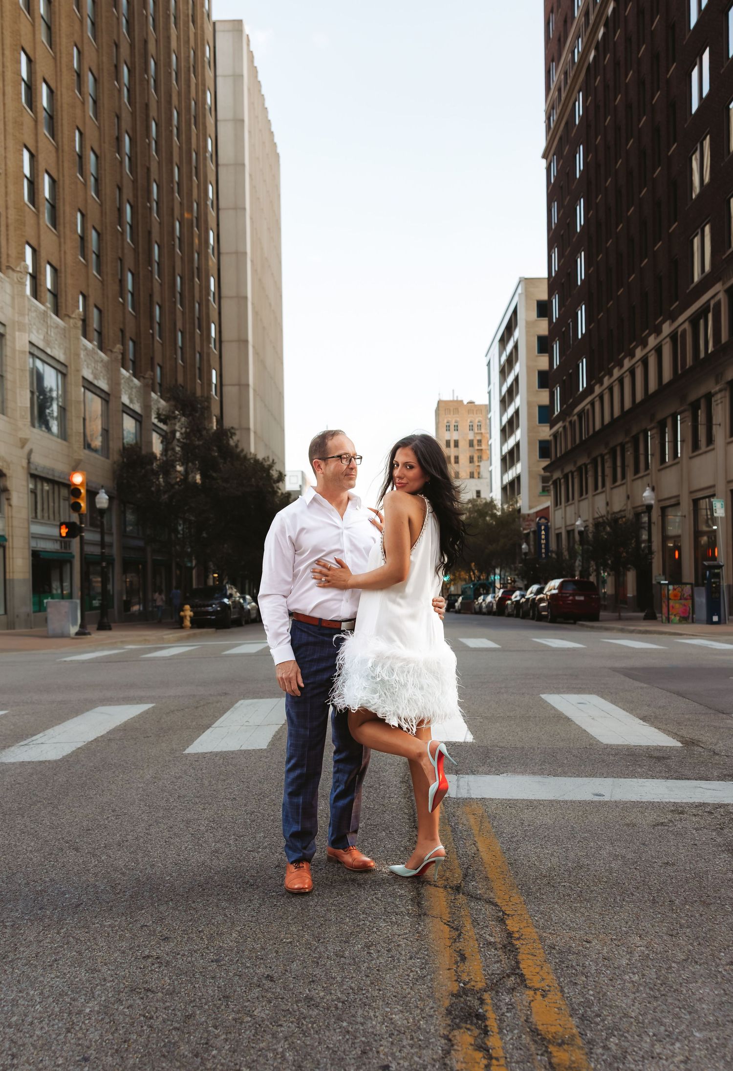 Couple posing together in white outfits at a downtown city intersection during golden hour. Tulsa Photographer