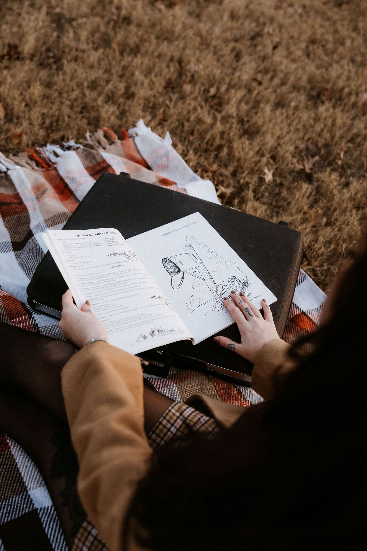 Woman reading illustrated book on plaid blanket in autumn field, overhead perspective view. Tulsa Photographer