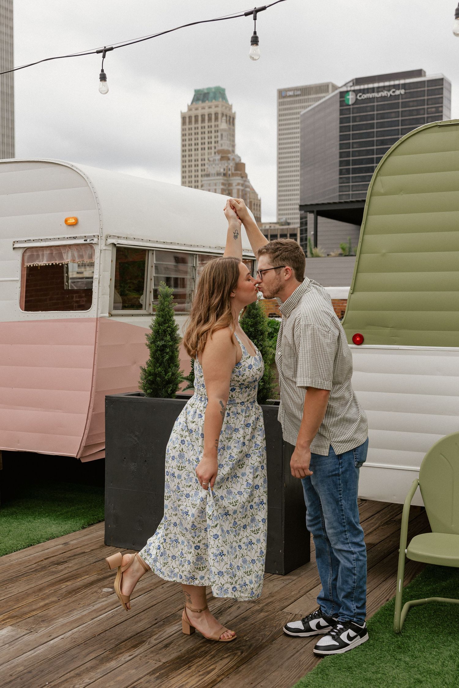 Couple dancing on rooftop deck with vintage trailers and city skyline backdrop.