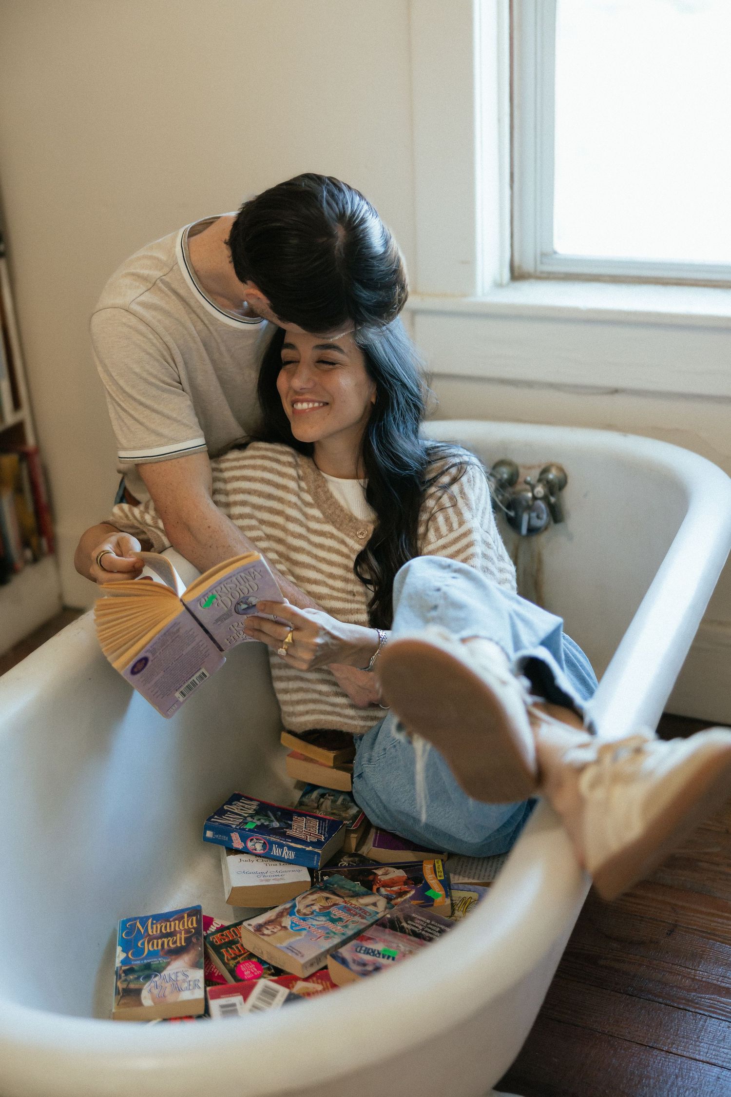 Couple sitting in a clawfoot bathtub filled with books, sharing a romantic moment while reading together.