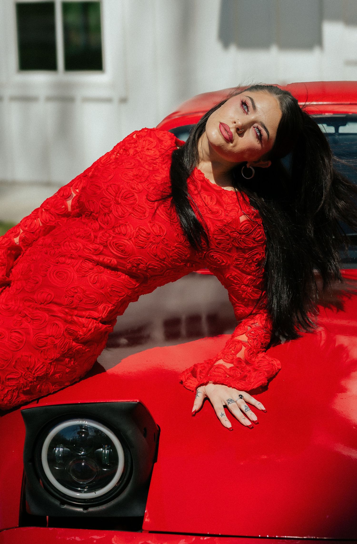 Woman in red lace dress posing dramatically on the hood of a red vintage car outdoors. Tulsa Photographer