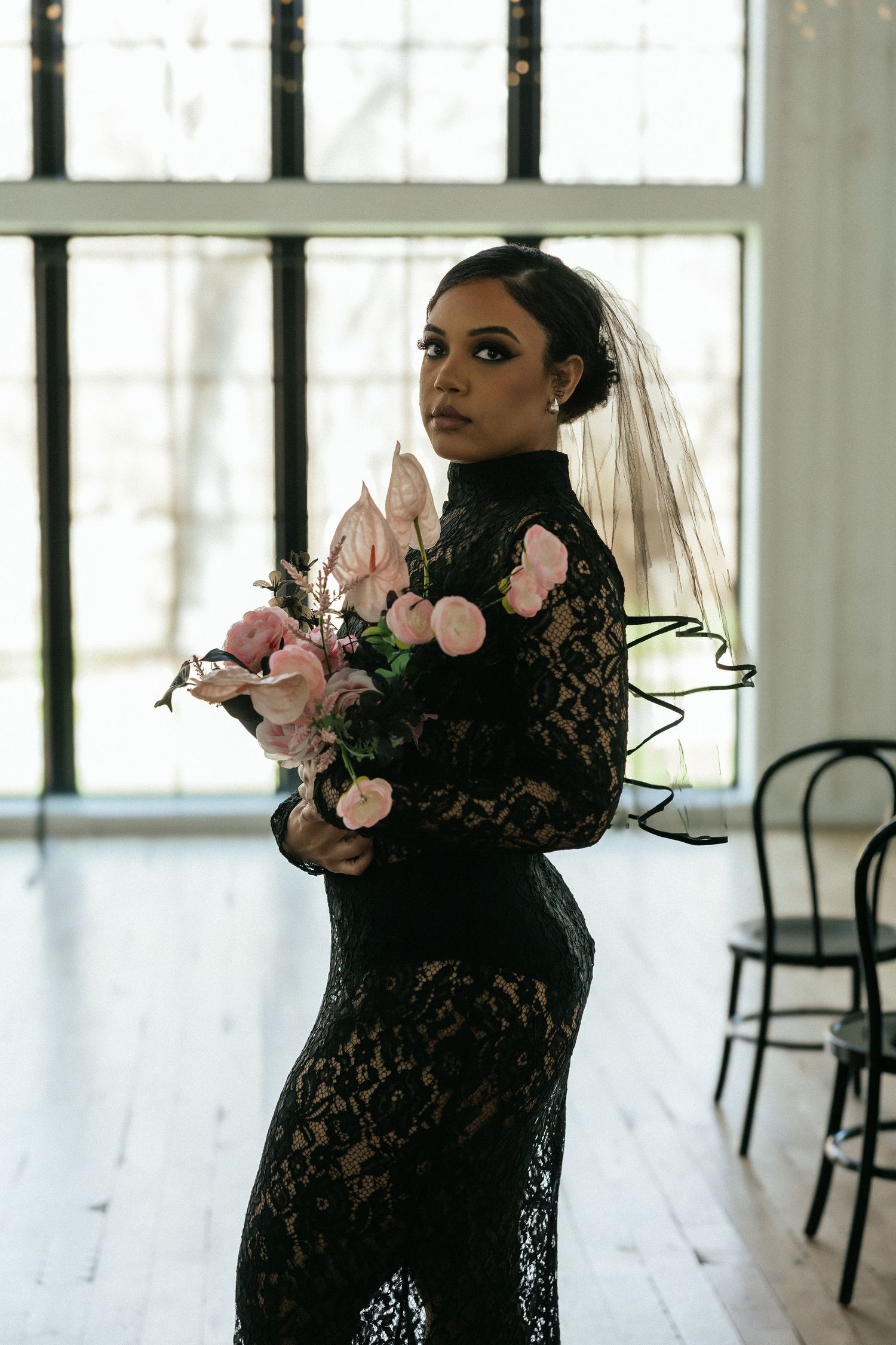 Bride in black lace wedding dress with veil holding pink floral bouquet in bright airy venue. Tulsa Photographer