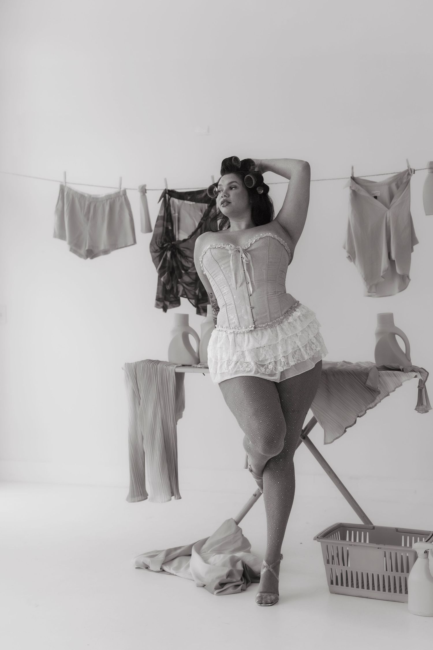 Black and white pin-up style photo of a curvy woman in corset and bloomers posing near a clothesline. Tulsa Photographer