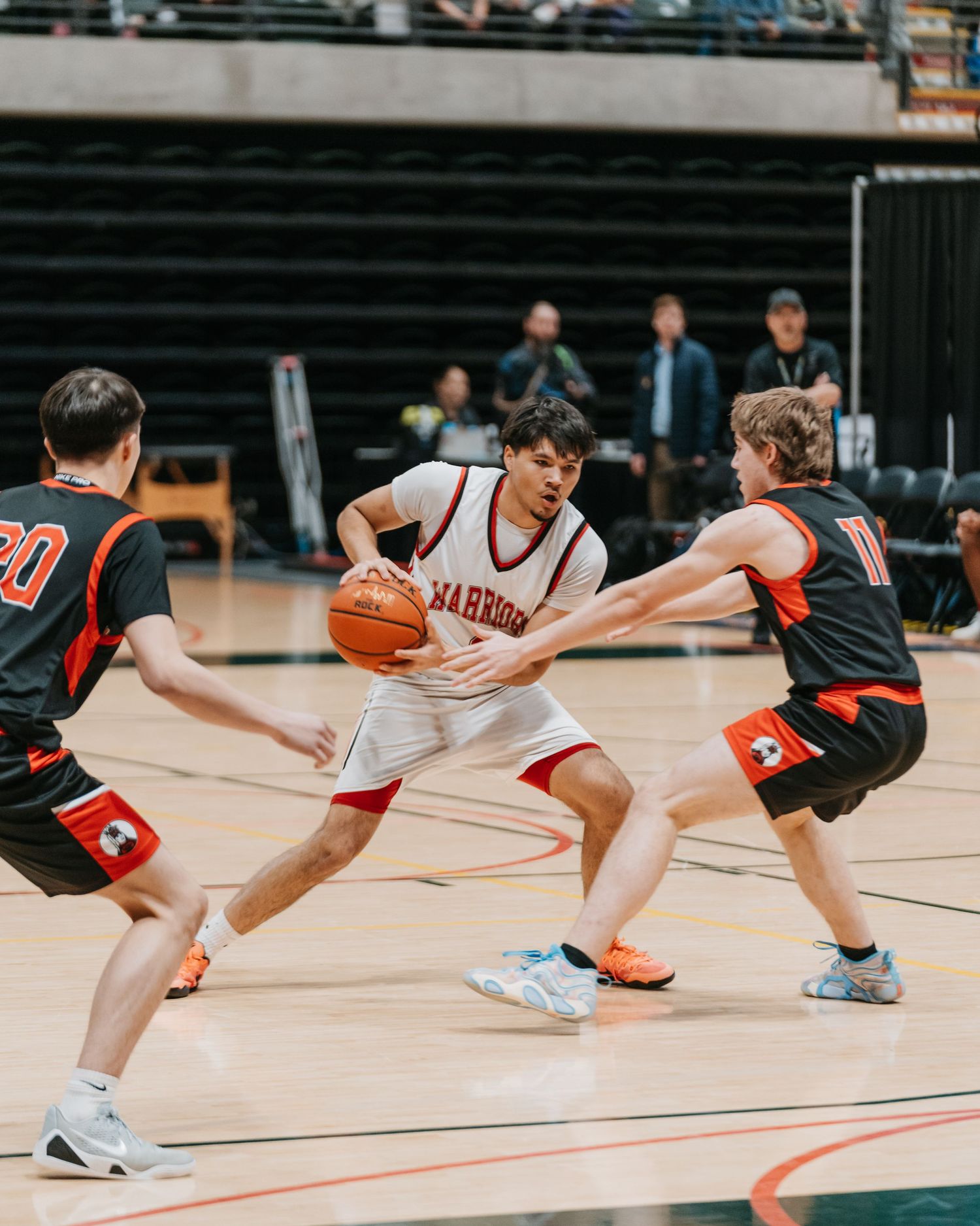 High school basketball player in Warriors jersey drives between two defenders on a hardwood court. Anchorage-sports-Photographer
