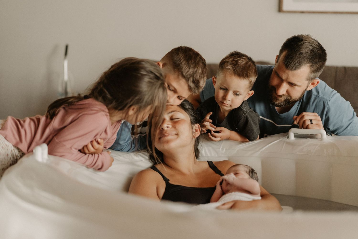 Emotional newborn moment as family gathers around mother holding her new baby on a hospital bed. anchorage-birth-photographer