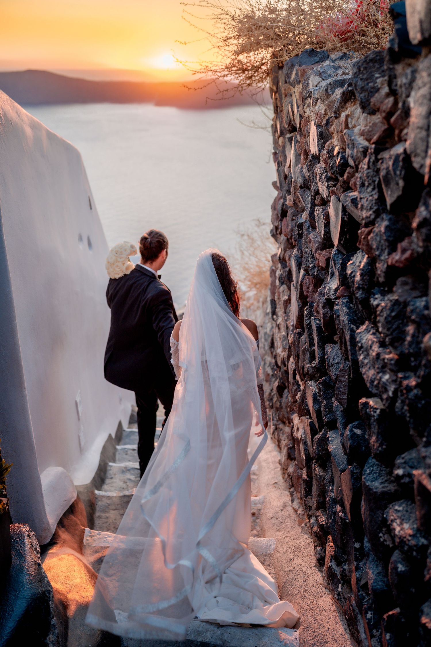 Bride and groom walking hand in hand in Santorini at sunset 🌅