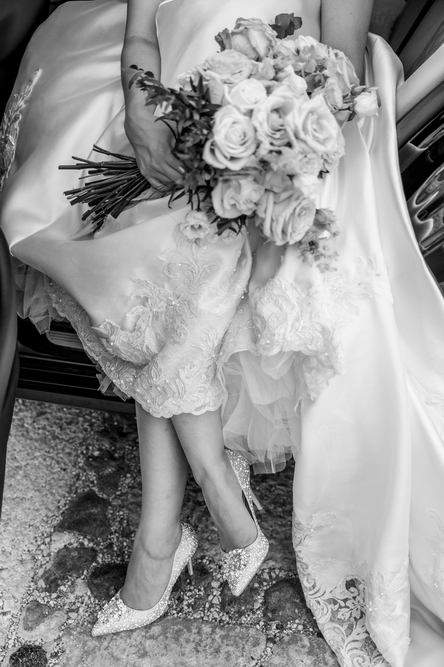 Bride in wedding dress and wedding shoes, holding an elegant flower-bouquet, sitting in a luxury car during a Santorini day-after session
