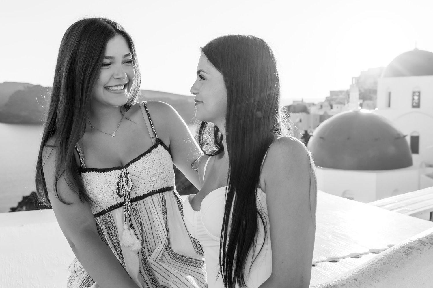 Joyful lifestyle photoshoot of two sisters on a Santorini terrace with a blue-domed background, natural light, family, and laughter