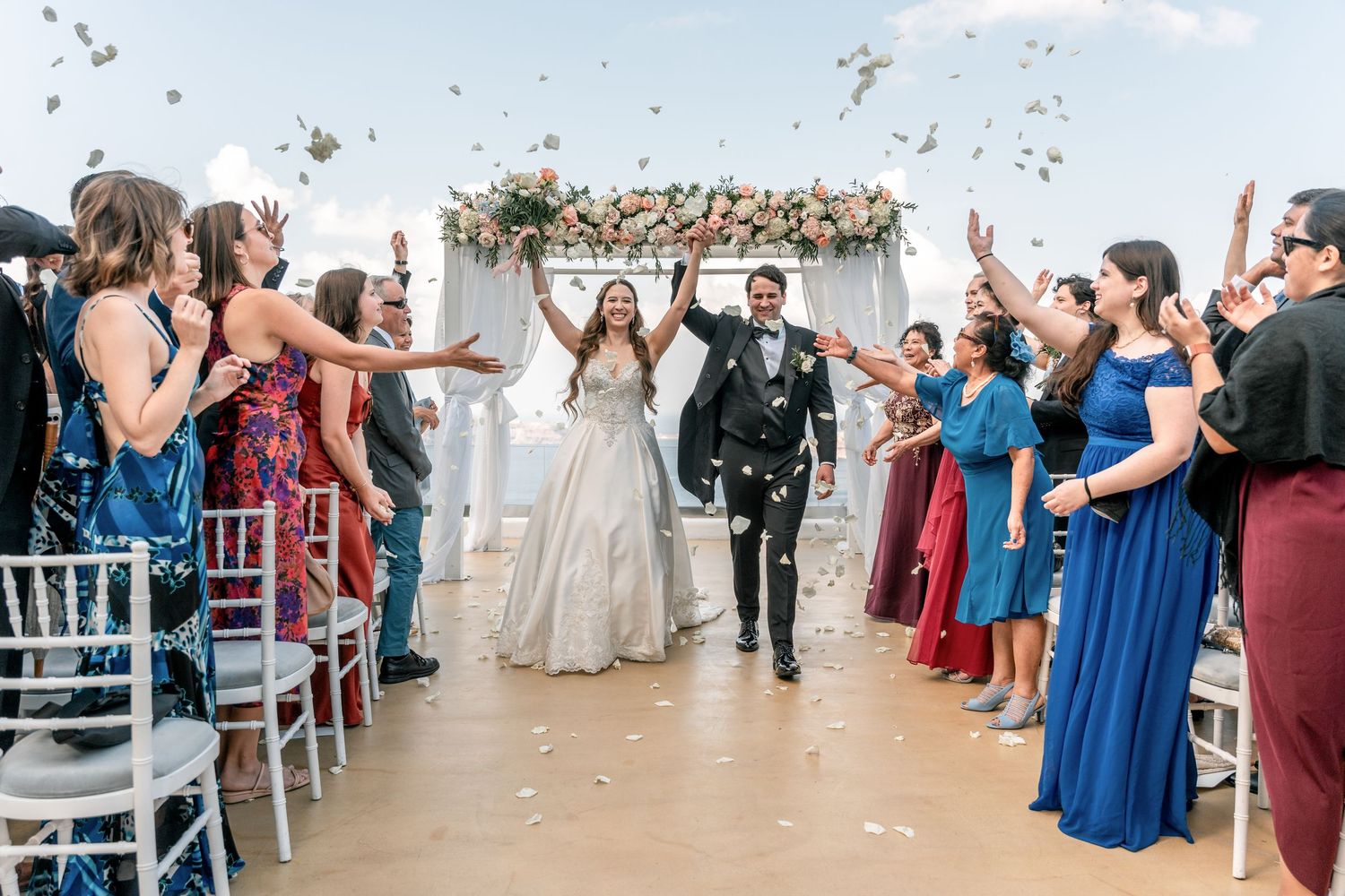 Bride in wedding dress, groom in suit, family, and guests captured at the end of wedding ceremonyon Santorini cliffs in venue after ceremony