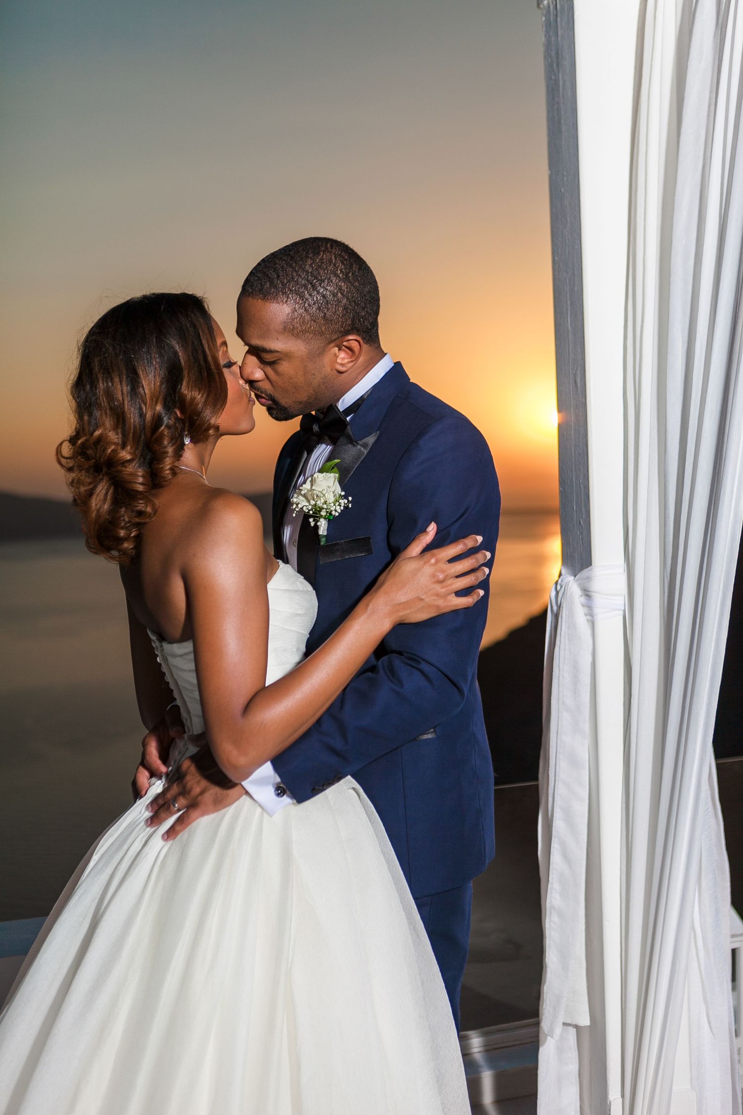 Bride in wedding dress, groom in suit, captured on Santorini venue during their ceremony at sunset